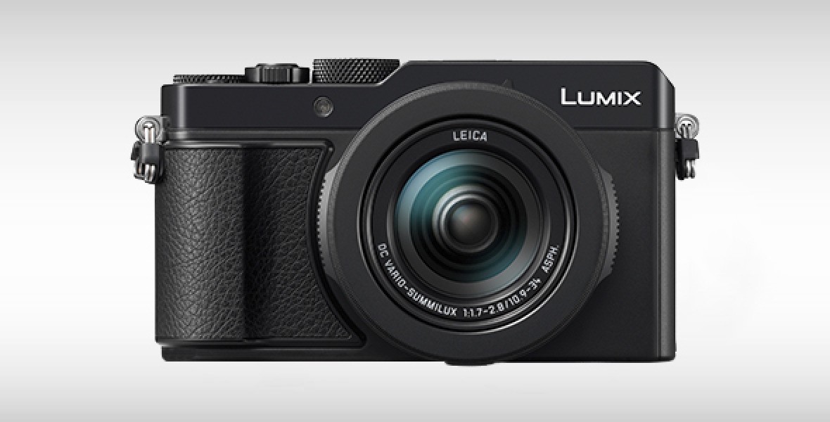 Schwarze Lumix-Kompaktkamera mit Leica-Objektiv vor grauem Hintergrund.
