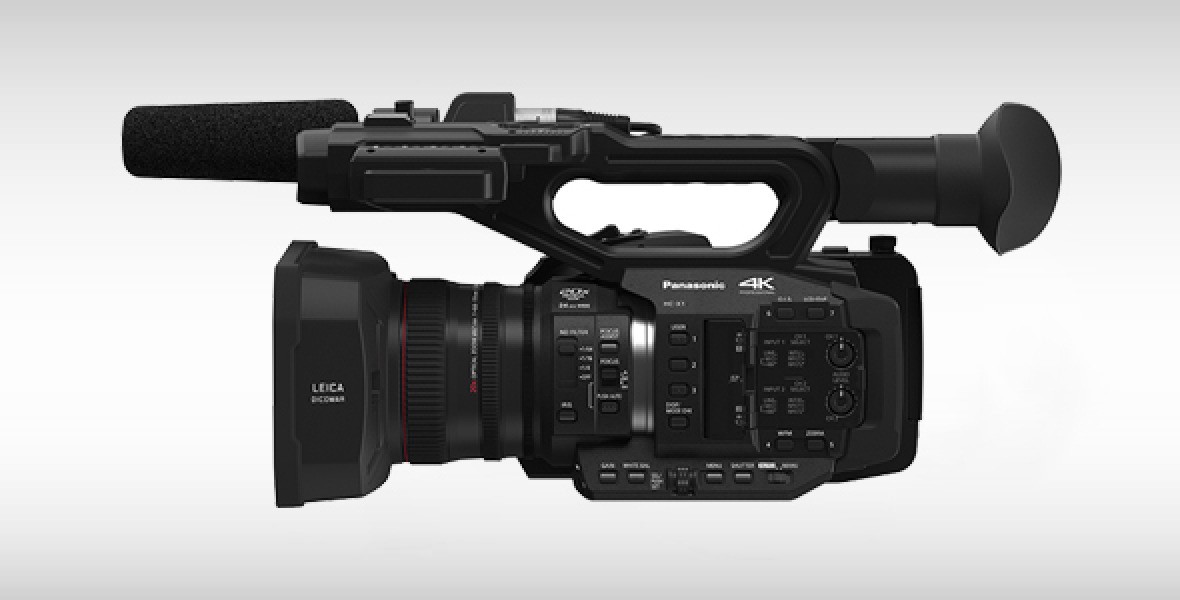 Professionelle Panasonic 4K-Videokamera seitlich, mit Objektiv und Mikrofon, gegen einen grauen Hintergrund.
